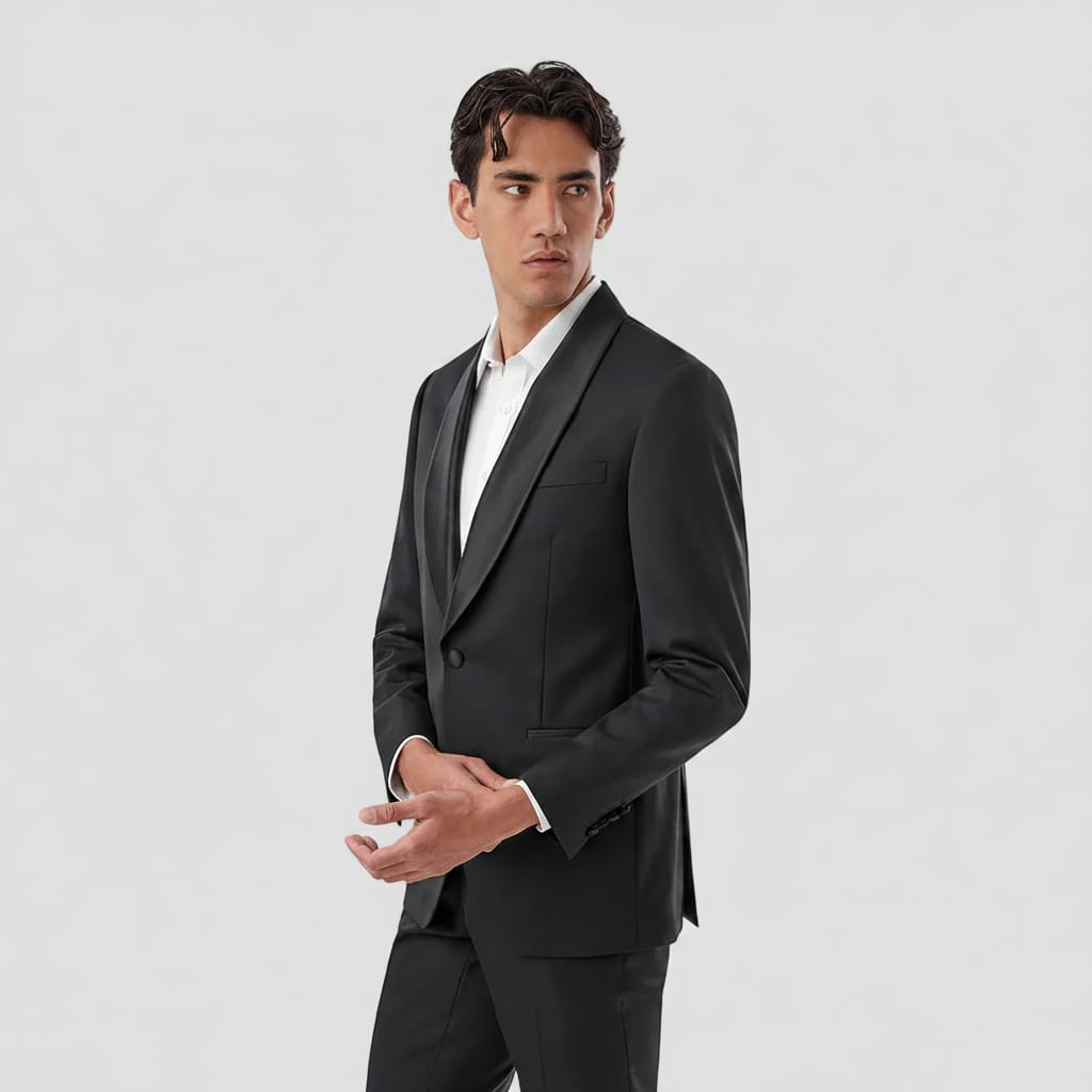 A man wearing a black shawl-lapel suit jacket with a white dress shirt, posed against a solid white background.