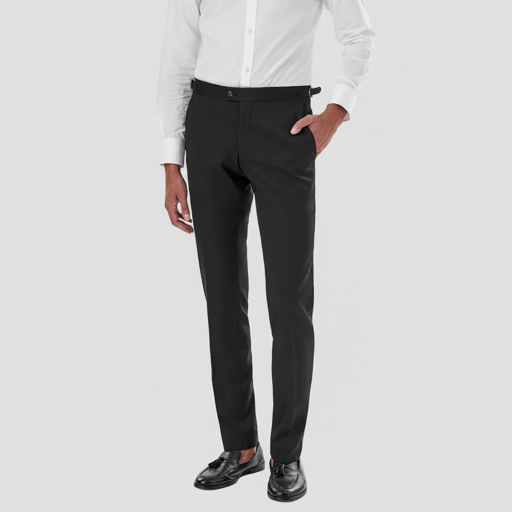 A man wearing black slim-fit dress pants, styled with a white dress shirt and black leather loafers, shown from the waist down on a white studio background.