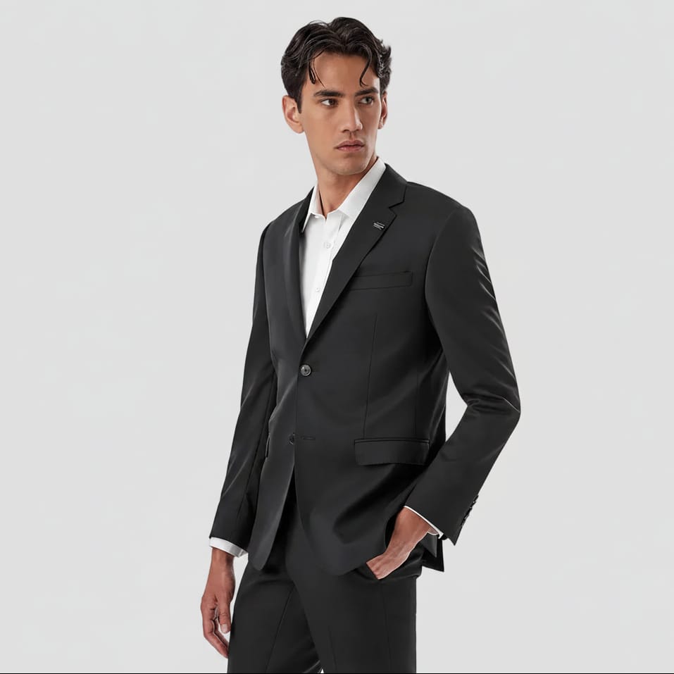 A man wearing a dark charcoal gray two-piece suit with a white dress shirt, standing against a solid white background.