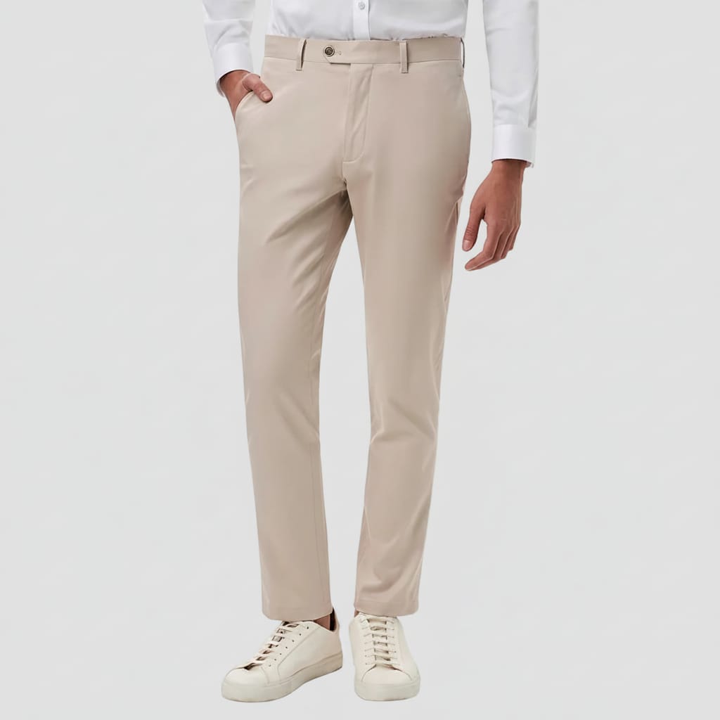 A person wearing slim-fit stone chinos with a white dress shirt and white sneakers, shown from the waist down against a plain white background.