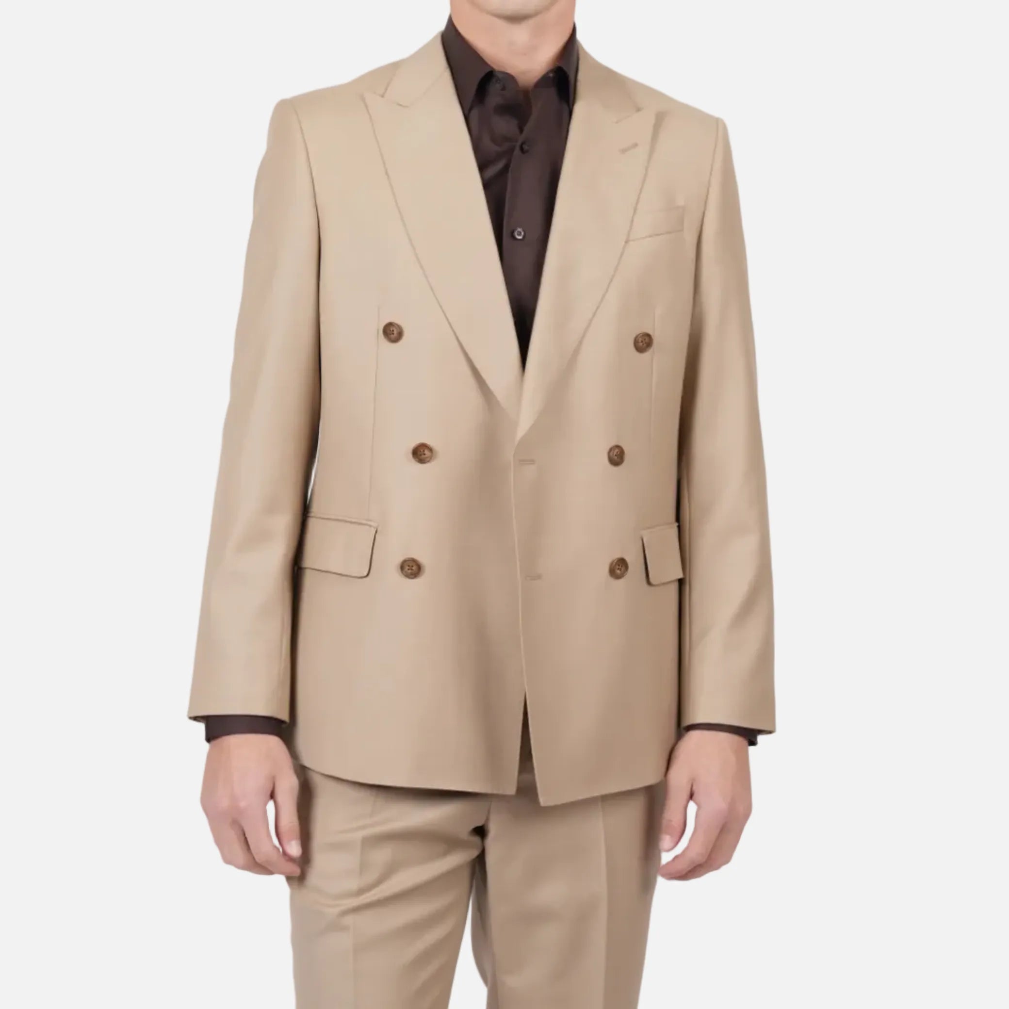 A man modeling a beige double-breasted suit with brown buttons, worn over a dark brown shirt, against a light gray studio background.
