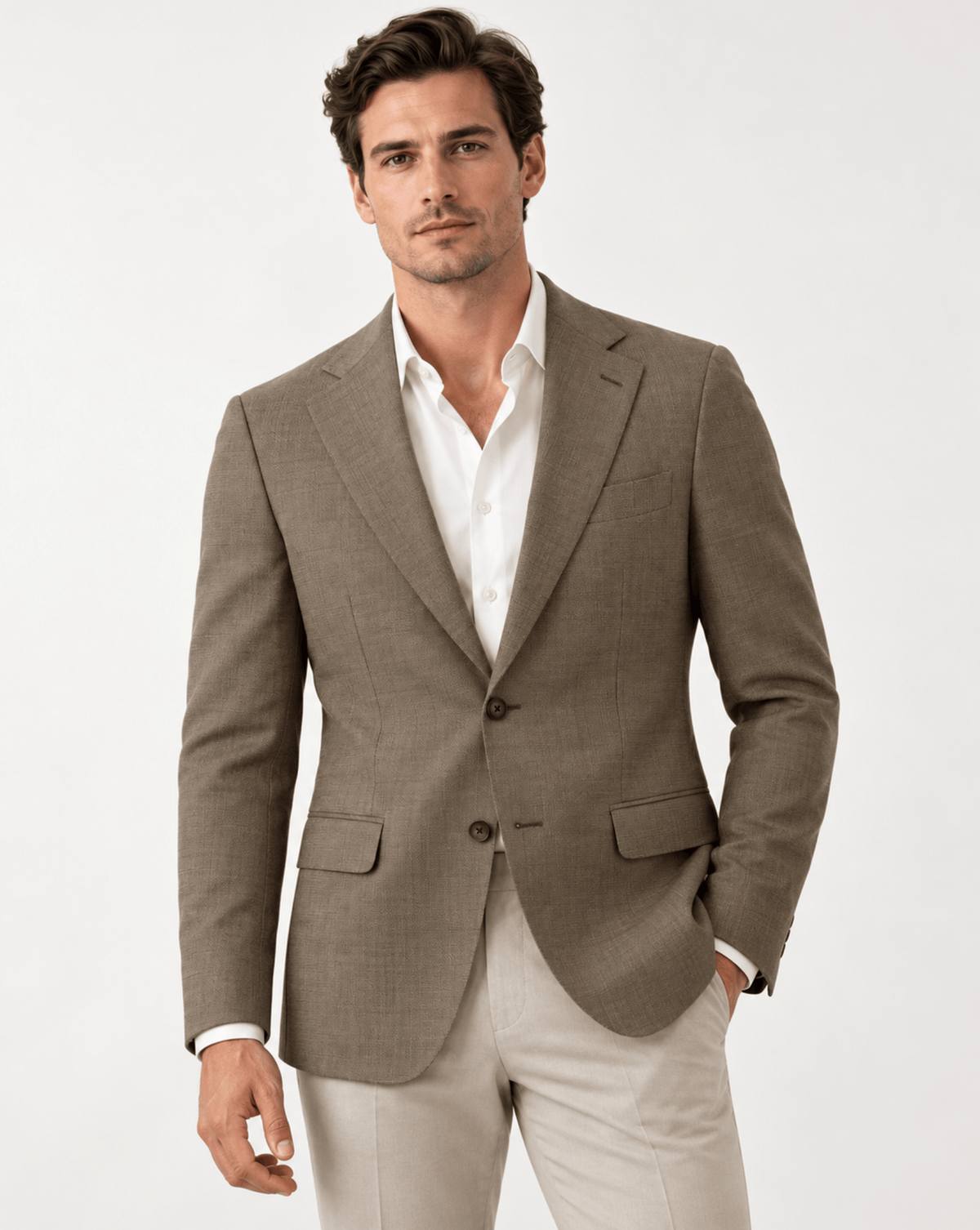 A man wearing a tailored light brown blazer over a white dress shirt and light beige trousers, photographed against a clean white studio background.