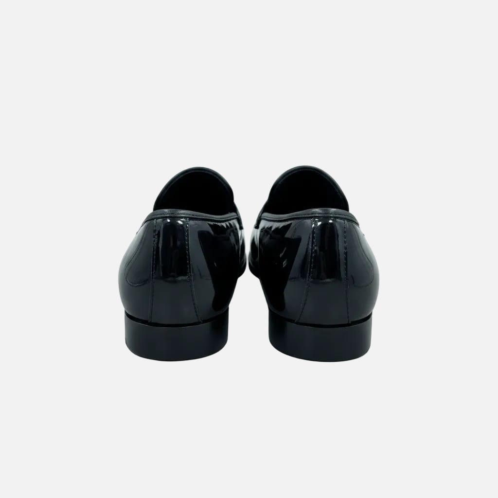 A pair of black patent leather loafers shown from the back, resting on a wooden table in what appears to be a retail or office setting.