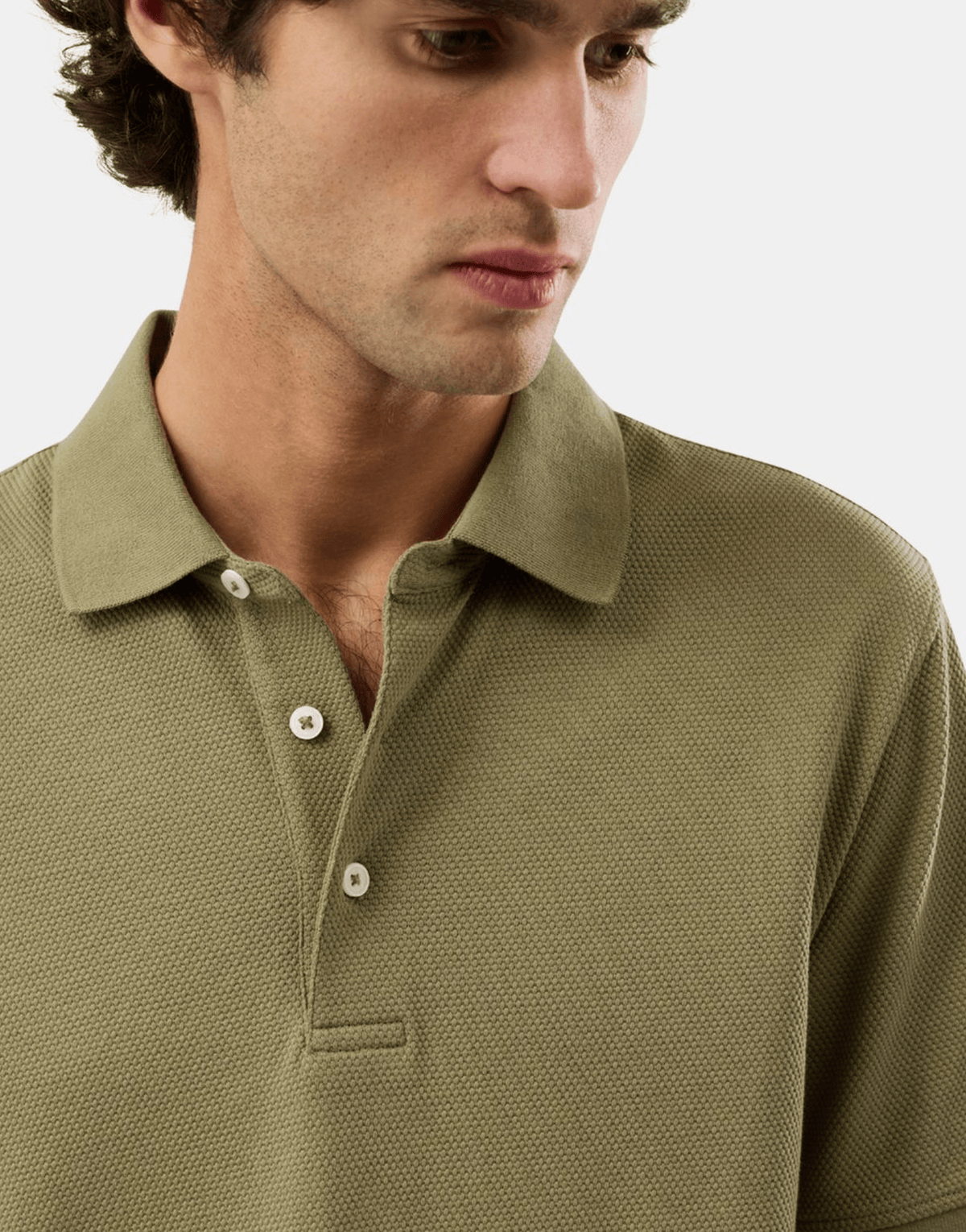 Close-up of a man wearing a textured olive green polo shirt with a collar and three-button placket, photographed against a light gray studio background.
