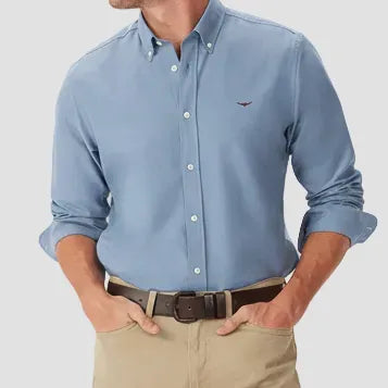 Man wearing a light blue button-up shirt and beige pants on a light gray background