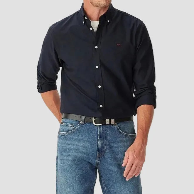Man wearing a navy button-up shirt and blue jeans on a white background