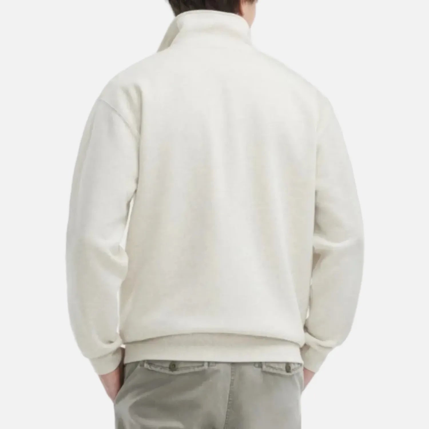 A man viewed from the back wearing a cream-colored quarter-zip mock neck sweater and light gray trousers, set against a plain light gray background.