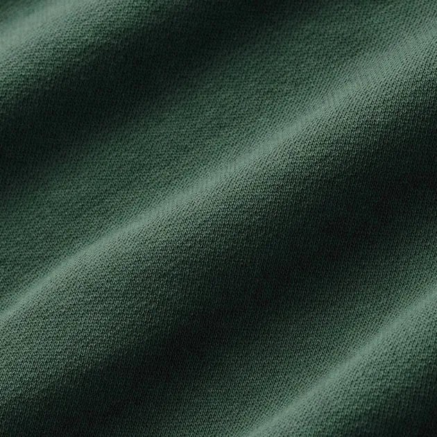 A close-up of dark forest green knit fabric with soft diagonal folds and a fine textured weave.