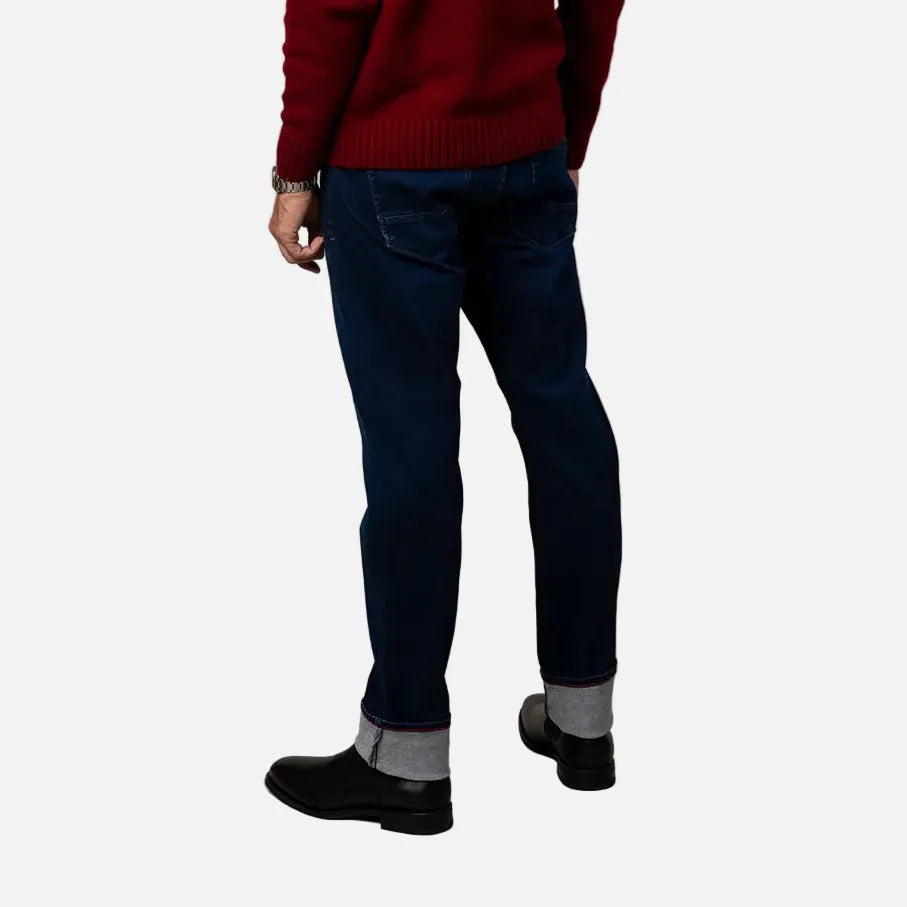 A man is shown from behind wearing a deep red knit sweater, dark blue jeans, and black shoes against a plain beige studio background.