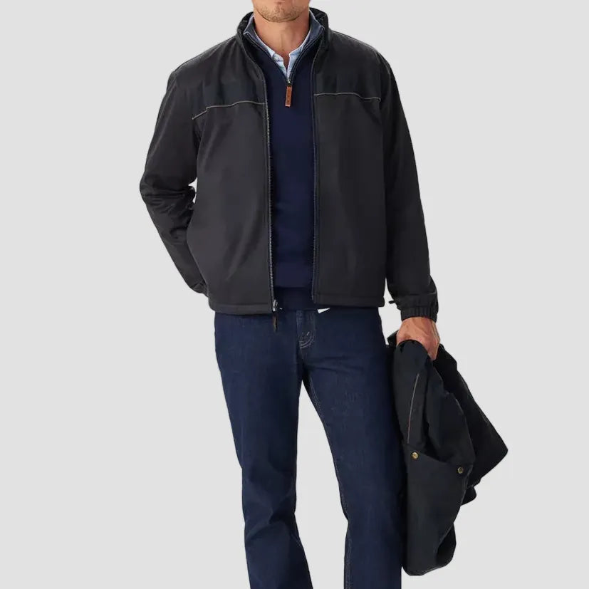 Man wearing a dark jacket, blue shirt, and jeans holding a coat on a white background