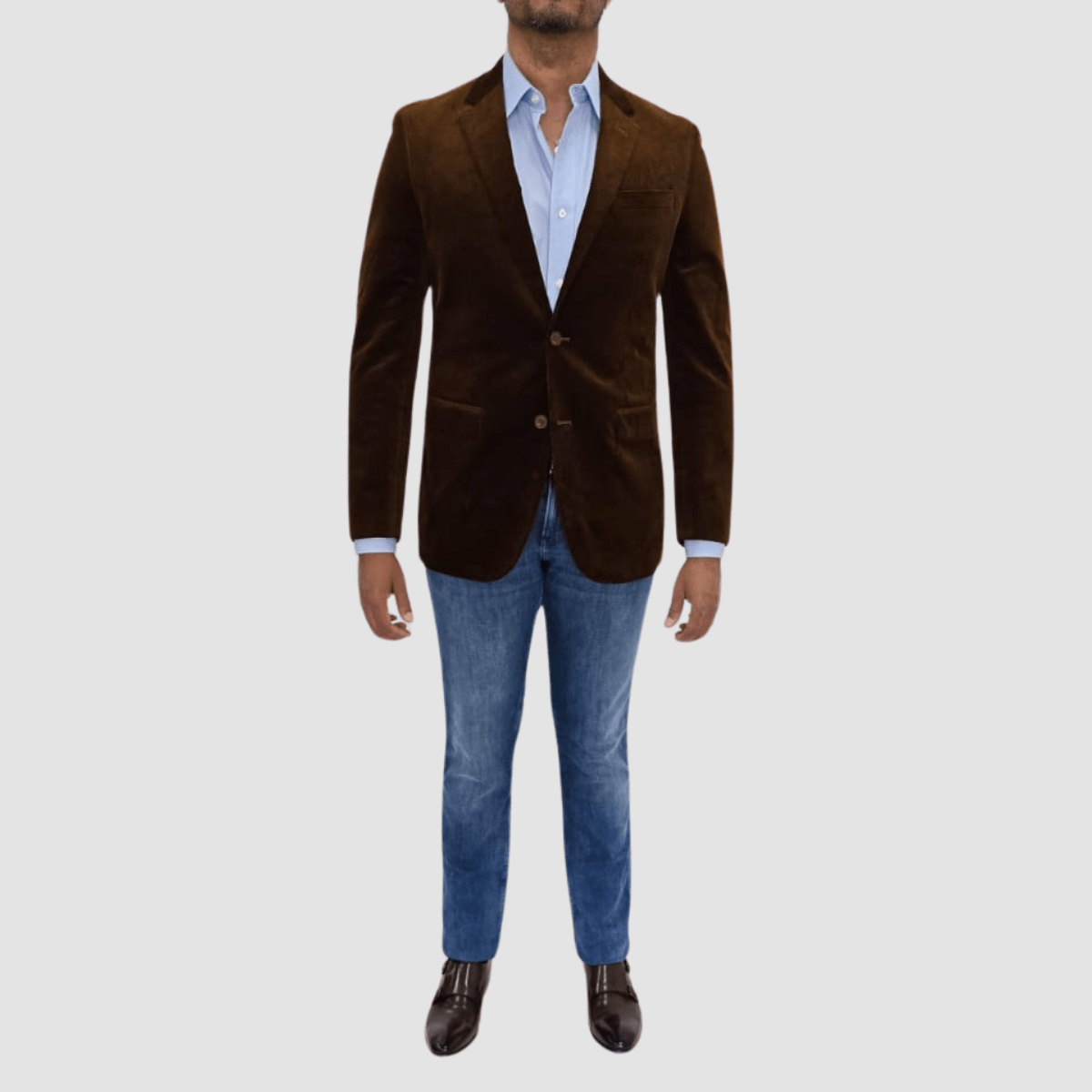 A man wearing a camel-colored, tailored-fit, cotton corduroy sports jacket with a notch lapel, two-button closure, and flap pockets. He is also wearing blue jeans and brown shoes.