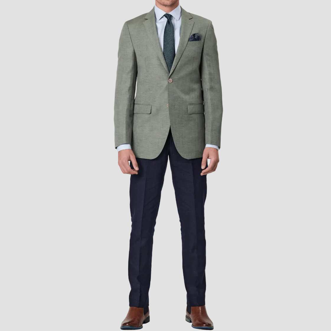A man wearing a green slim fit sports jacket with notch lapel, double button closure, and welt chest pocket, paired with navy pants, dark green tie and pocket square.