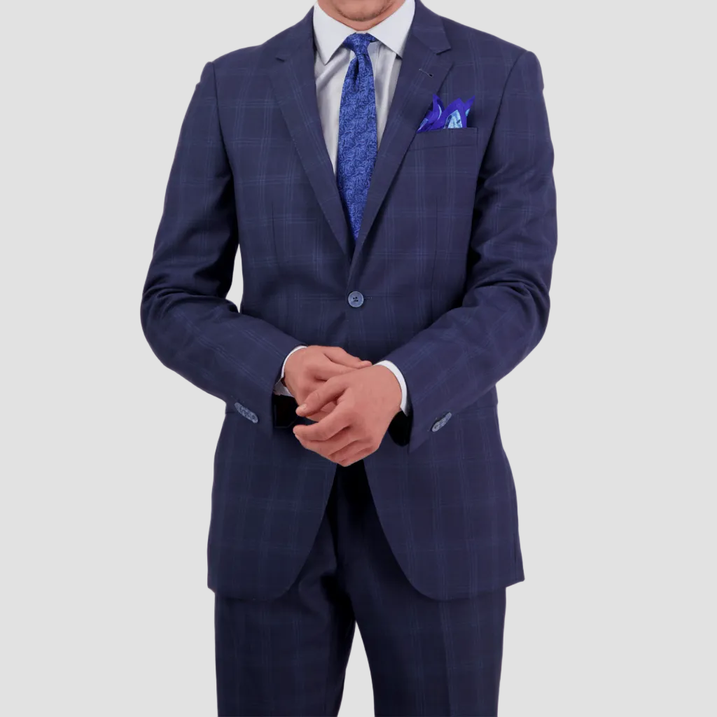 A man wearing a tailored fit cornflower blue wool cashmere suit by Savile Row, with a windowpane check pattern, featuring a notch lapel, two buttons, and a double vent. Complimented with a white shirt, blue tie and pocket square.