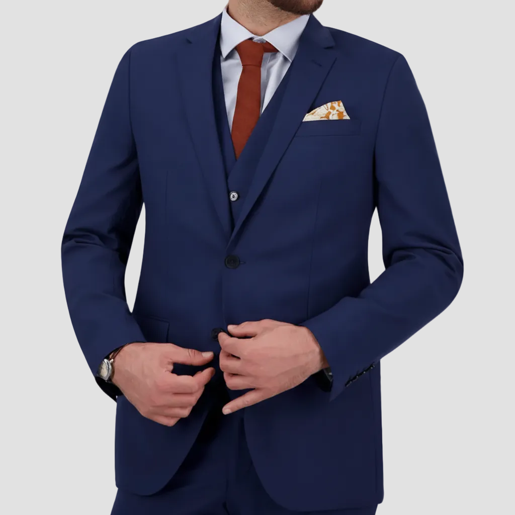 A denim blue tailored fit men's suit from Savile Row with a double button design, light shirt, red tie and pocket square.