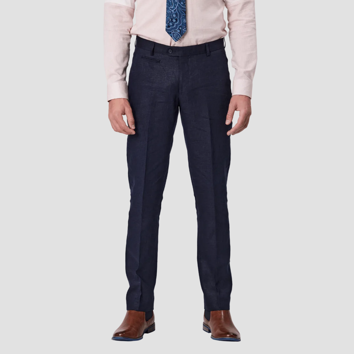 A man wearing navy linen tailored fit trousers and a pink dress shirt, paired with brown leather shoes.