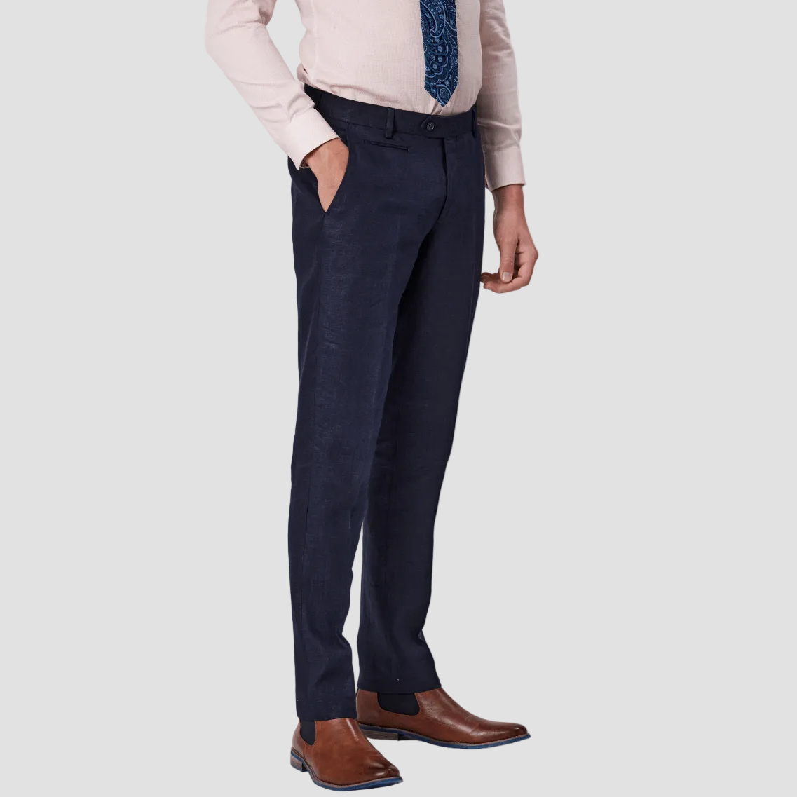 A man wearing navy linen tailored fit trousers and a pink dress shirt, paired with brown leather shoes.