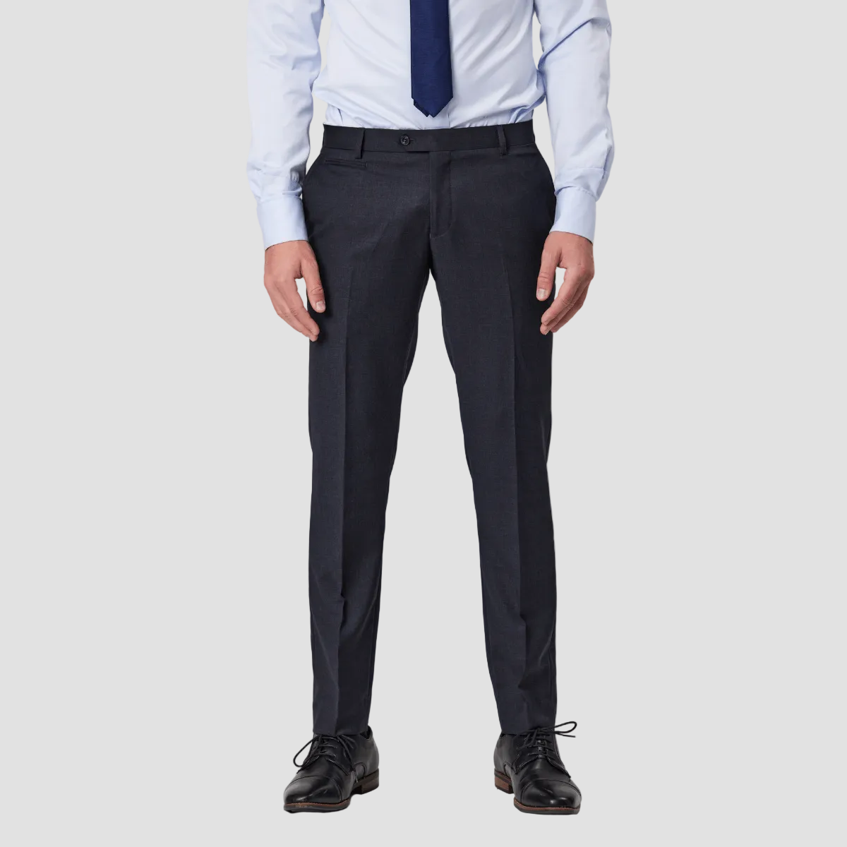 A man wearing slim fit wool blend charcoal gray pants by Savile Row and trousers with a light blue shirt and a navy blue tie.