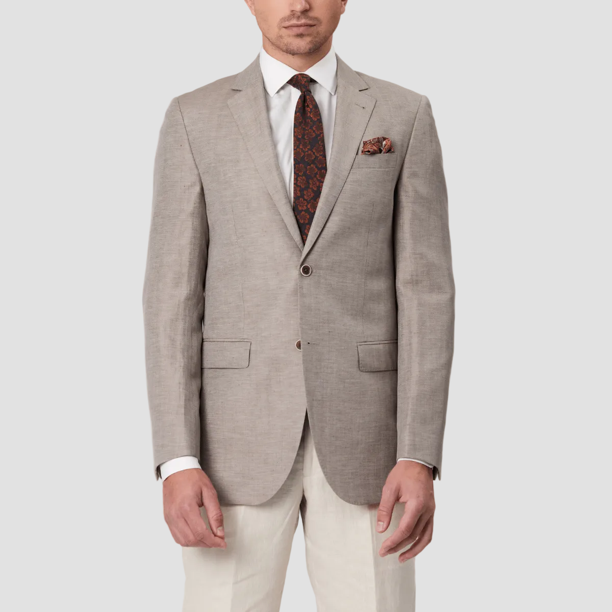Man wearing a beige suit with a white shirt and patterned tie and pocket square, with cream pants.