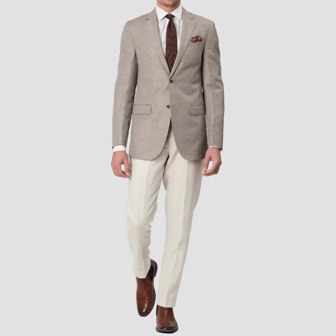 Man wearing a beige suit with a white shirt and patterned tie and pocket square, with cream pants.
