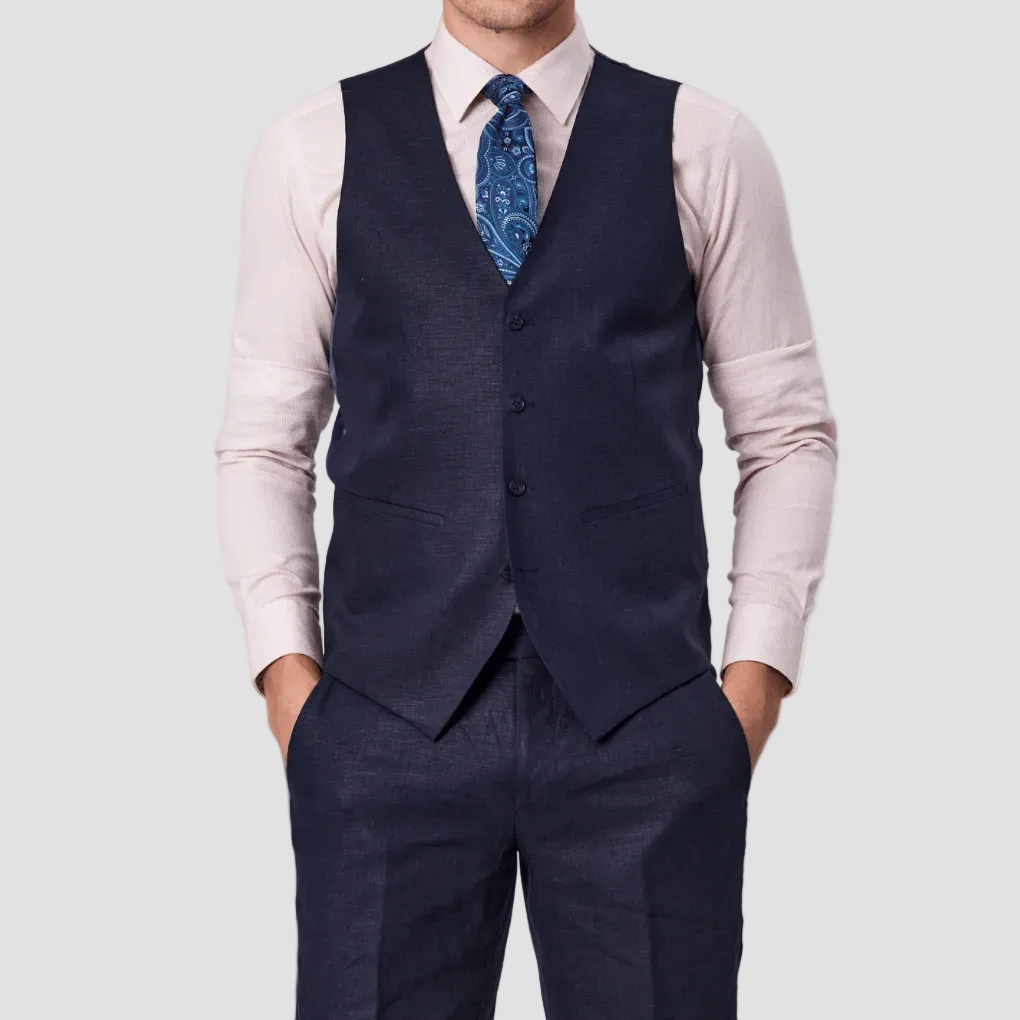 A man wearing navy linen tailored fit vest, a pink dress shirt and blue patterned tie.