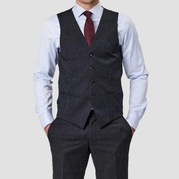 Man wearing a patterned charcoal gray suit vest by Savile Row over a light blue shirt with a red tie.