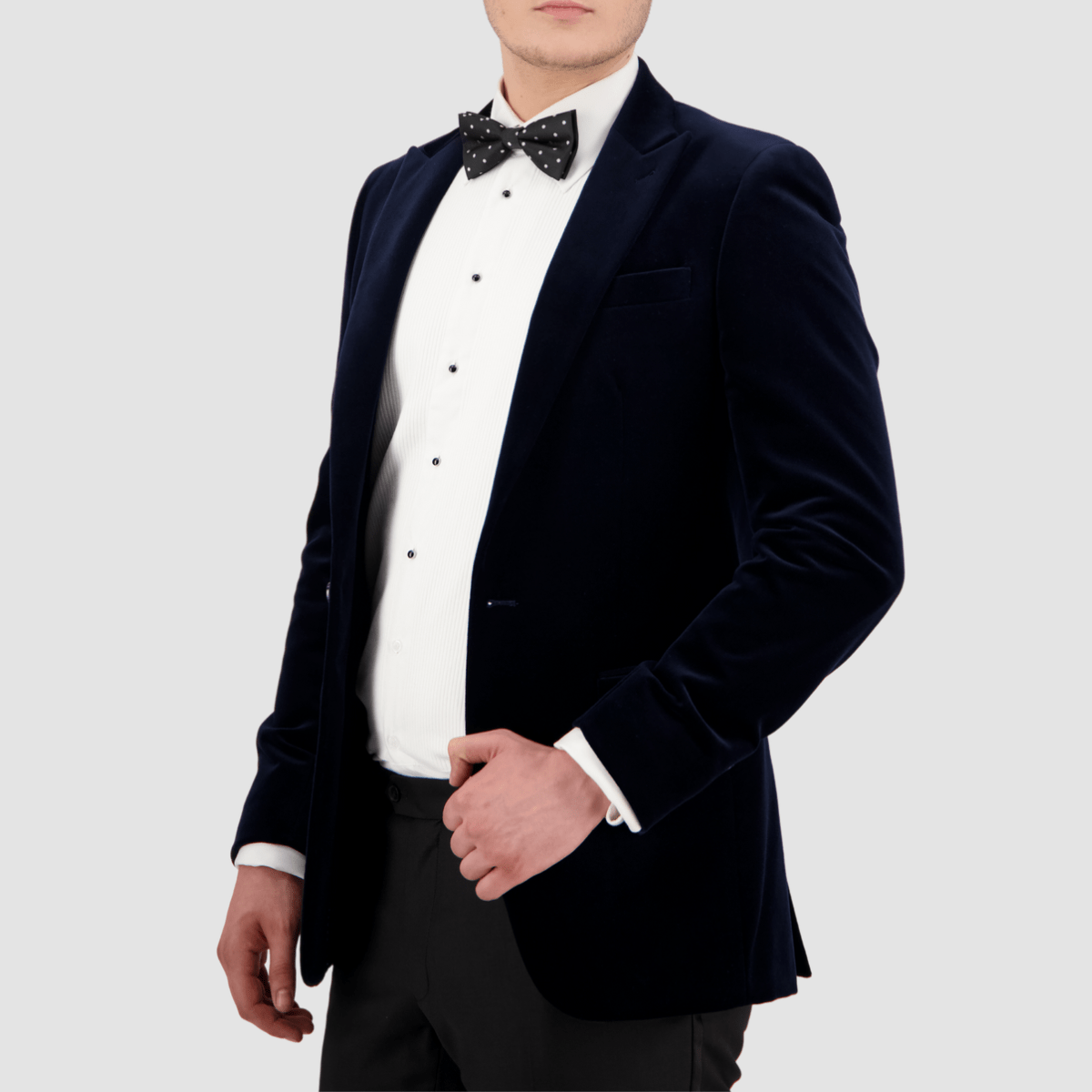 A man wearing a navy velvet sports jacket with a slim fit and peak lapel by Savile Row, paired with a white shirt and a bow tie.