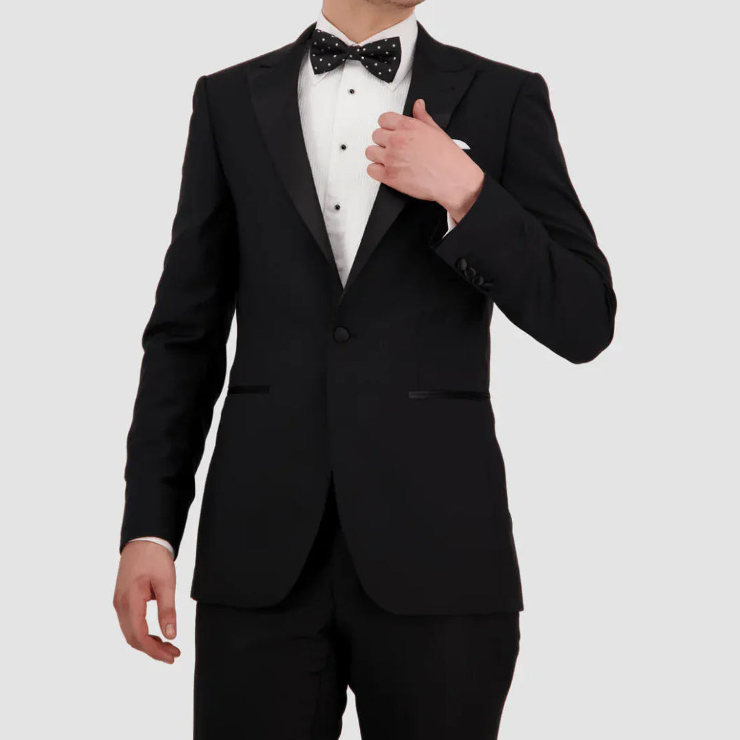 Man wearing a black tuxedo with a white shirt and bow tie on a light gray background