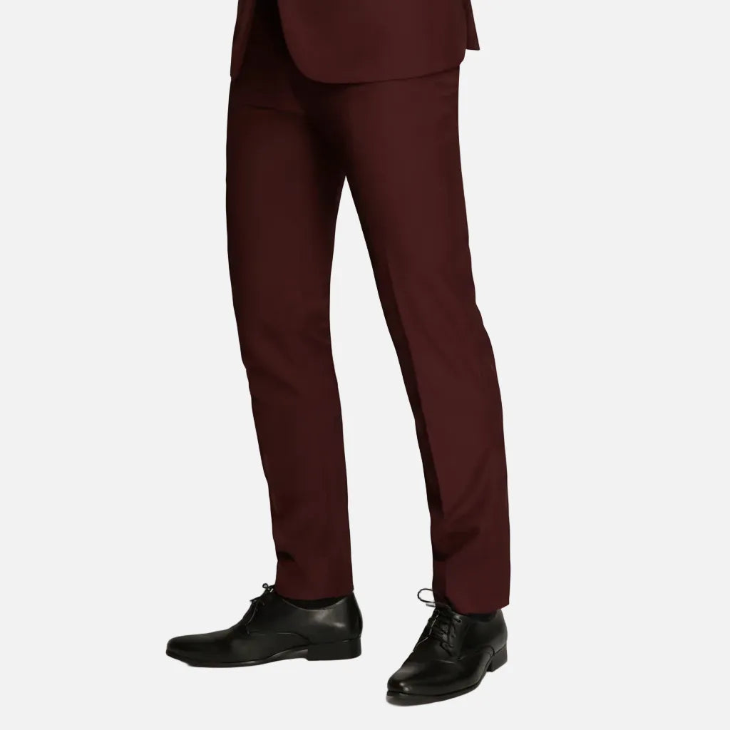 A person wearing slim-fit burgundy trousers with black leather dress shoes, shown from the waist down against a plain light gray studio background.
