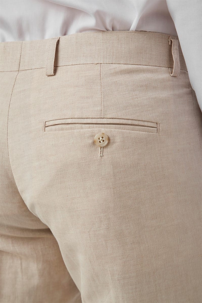 Close-up of beige pants with a button detail, worn with a white shirt.