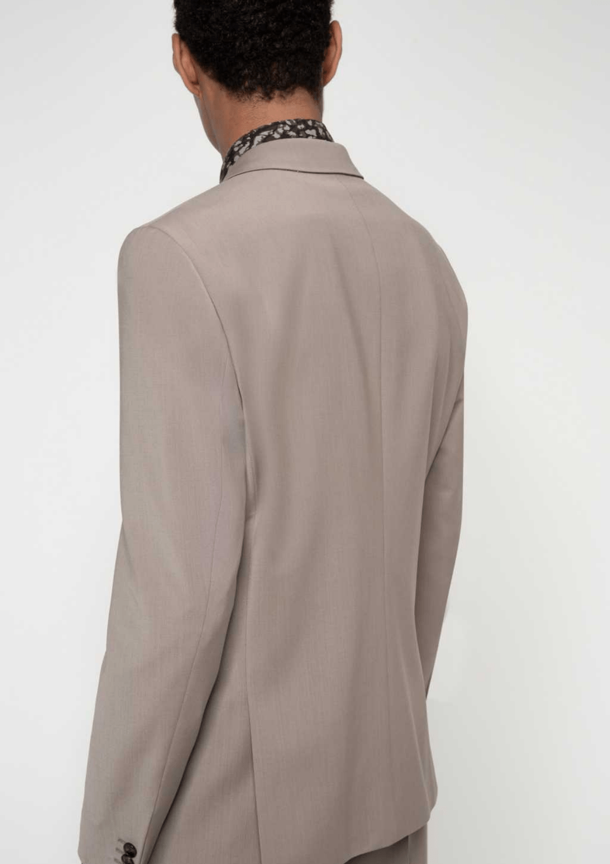 a light beige suit jacket on a model who is facing the back, the jacket is slim fitting with brown buttons on the cuff