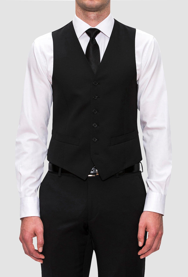 a front view of a model wearing the Joe Black slim fit mail vest in black pure wool with a white shirt and a black tie