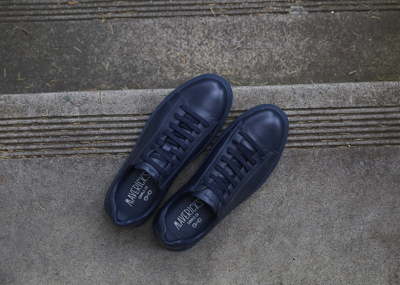 a top view of the mavericks mens leather sneakers in navy blue sitting on a concrete step