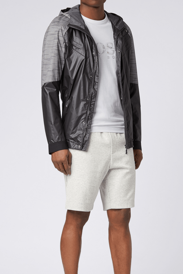 a model wears the mens hugo boss logo t-shirt in white 100% cotton with a grey windbreaker and knitted shorts