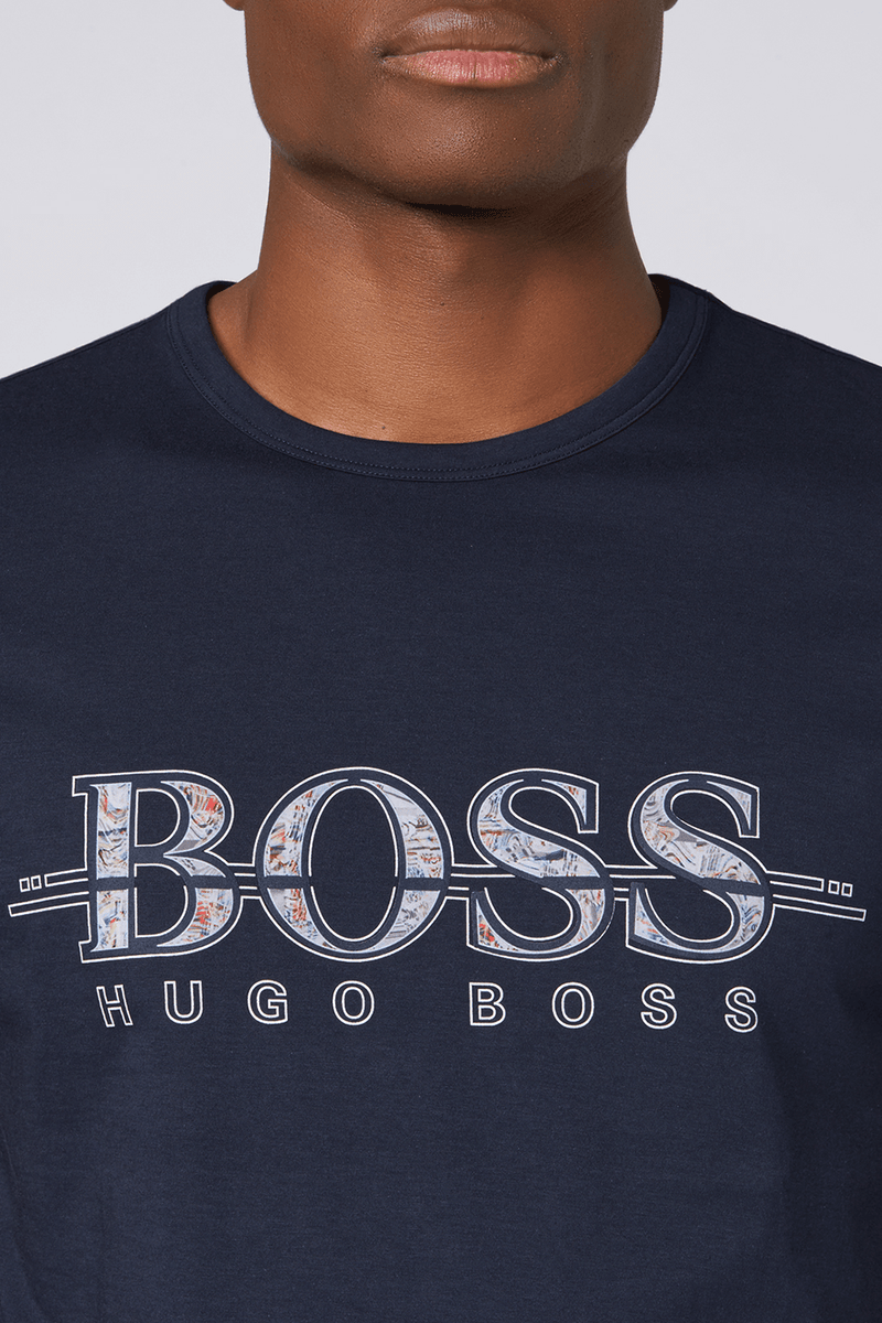 a close up view of the front logo on the tshirt with a cut out boss logo filled with a coloutful pattern and the words hugo boss underneath against a navy cotton background