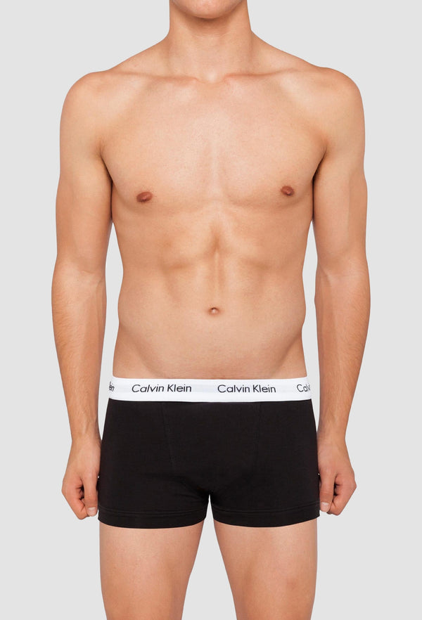 a model wears the Calvin Klein black cotton stretch trunk with a white waistband and Calvin Klein logo in black writing 
