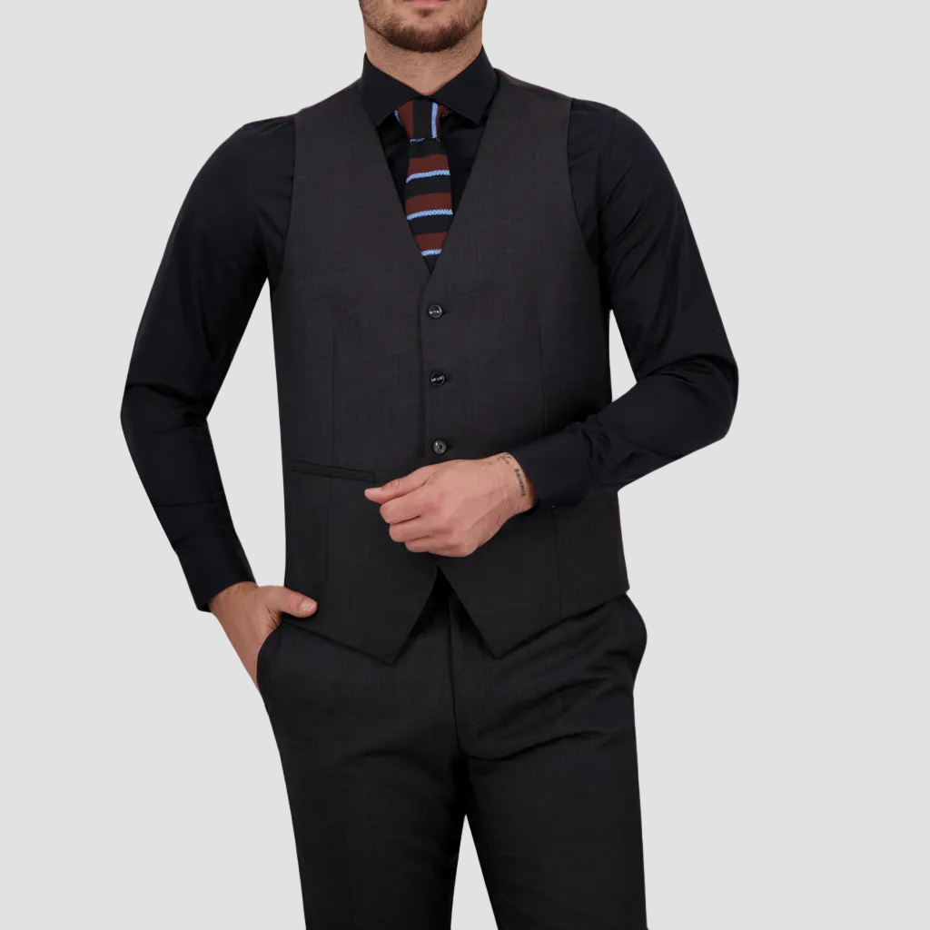 Man wearing a charcoal vest with matching pants by Savile Row and a black shirt with a patterned tie.